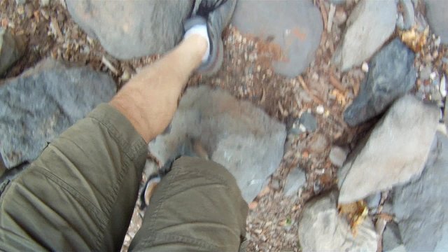 A hiker's point of view of his feet as he hikes near a stream