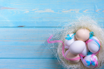 Easter eggs with colourfulll tapes and bow in nest over blue wood background. Top view with tag for copy space