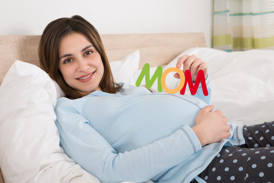 Pregnant Woman With Text Mom Lying On Bed