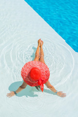 Woman sitting in a swimming pool in a sunhat