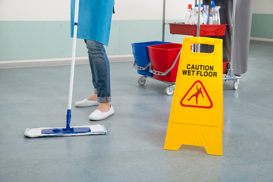 Female Janitor Mopping Corridor With Caution Sign