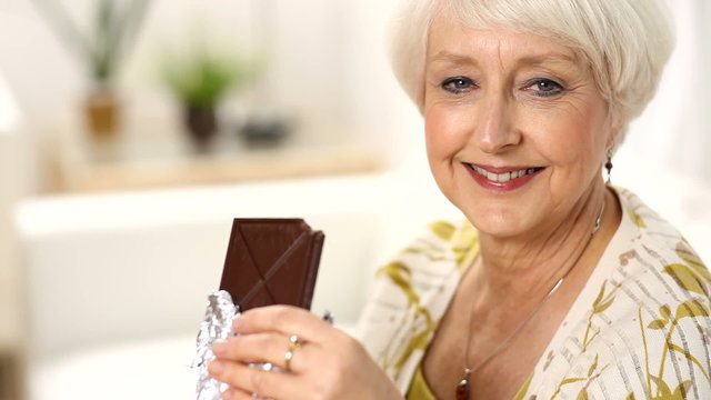 Senior woman takes bite of chocolate bar