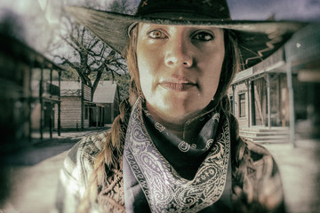 Old West Cowgirl Eyes Western Town. Old west cowgirl looks into camera with western town setting in...