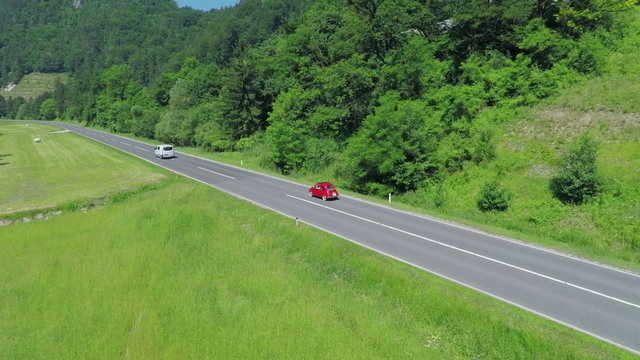 Two modern cars passing a small red vintage car