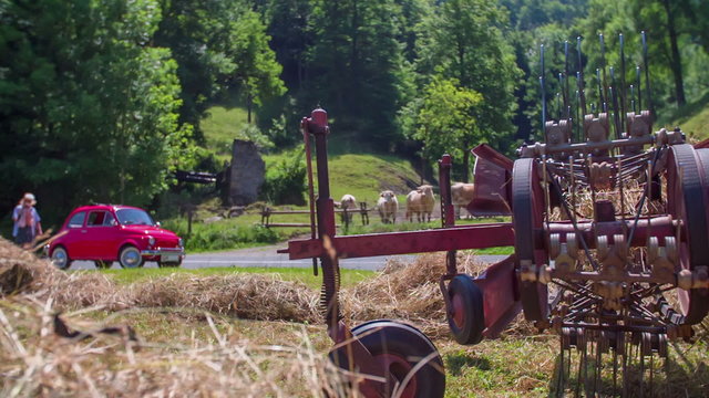 An older couple standing next to their red vintage car at the side of the road