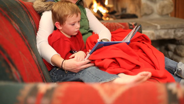 Mom reading son book by fireplace