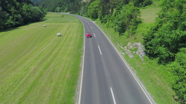 Small red car driving, motorcyclists passing by