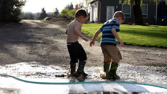 Two young boys playing in mud puddle