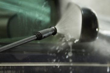 Closeup high pressure water cleaner as seen spraying on car side mirror and window