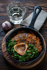 Frying pan with ossobuco and a glass of white wine, close-up