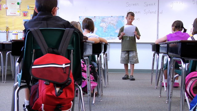 Student standing up in front of class reading paper