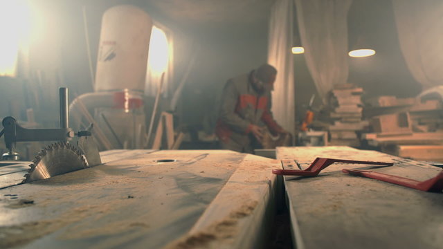 Man bringing the piece of wood to bench saw 