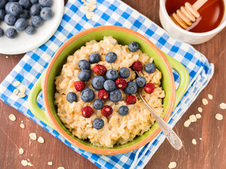 Oatmeal porridge in a green bowl with blueberries and wild strawberries on checkered napkin