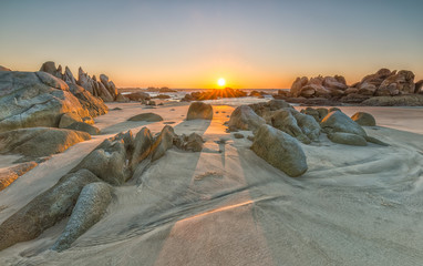 Naklejka premium The path of the rock into the sun rises with volcanic rocks on the sand overlooking the sea where the sun was rising star radiating beautiful to watch