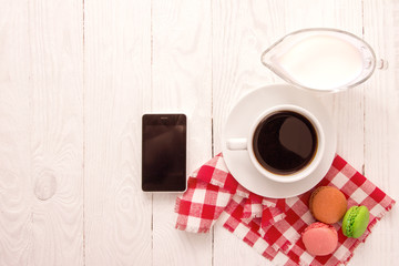 Colorful macaroons and a cup of coffee with cellphone on wooden table