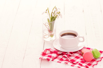 Colorful delicious macaroons on a plate and a Cup of coffee on a wooden table with flowers in a jar of water