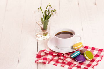 Colorful delicious macaroons on a plate and a Cup of coffee on a wooden table with flowers in a jar of water