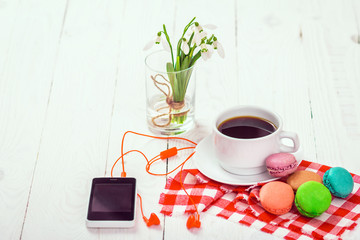 Colorful delicious macaroons on a plate and a Cup of coffee on a wooden table with flowers in a jar of water