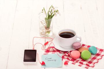 Colorful delicious macaroons on a plate and a Cup of coffee on a wooden table with flowers in a jar of water