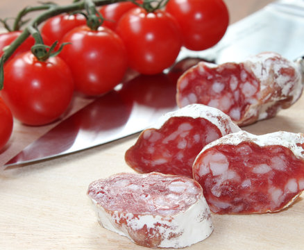 italienische Salami und Tomaten im Hintergrund auf einem Holzbrett