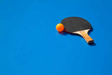 Orange ping pong ball with paddle on a blue tennis table