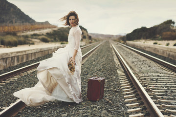 novia pensativa con una maleta roja en las vías del tren