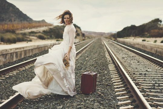 novia pensativa con una maleta roja en las v&iacute;as del tren