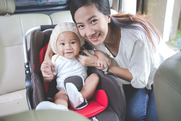 Fototapeta premium Mother securing her baby in the car seat in her car