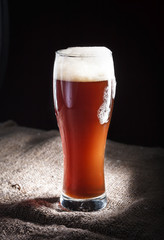 Close-up wet glass of dark beer  with foam on a burlap background 