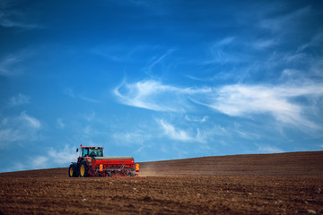 Farmer with tractor seeding crops at field