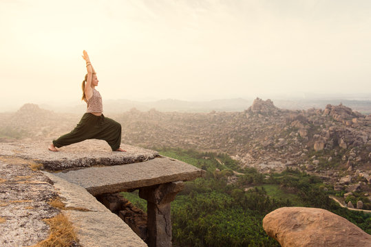 Young Woman Practicing Yoga At Mountain Cliff On Sunrise