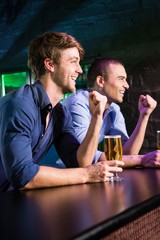 Two happy men raising their fist while having beer at bar counte