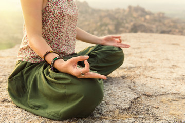 Young woman meditating at mountain cliff on sunrise. Hands close-up