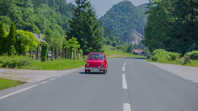 Small red vintage car making a curve on a country road