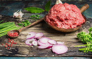 Chopped meat in pan with wooden spoon and ingredients for tasty cooking on rustic kitchen table