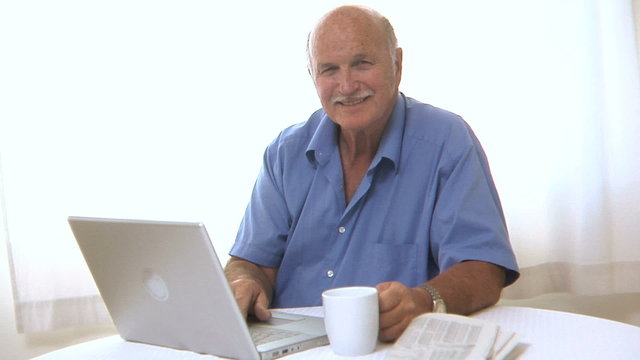 Senior man with laptop and newspaper