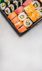 Sushi set with tuna nigiri, inside and outside rolls in transport box on gray stone background, top view, place for text, border