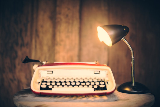 Vintage typewriter with lamp on wooden table at wooden wall back