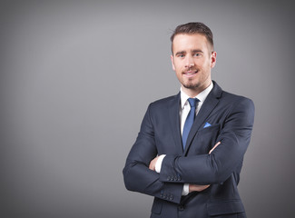Handsome businessman standing with arms crossed on grey backgrou