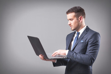 Handsome businessman holding a laptop on grey background