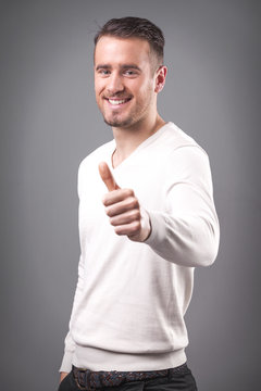Smiling casual guy showing thumbs up on grey background