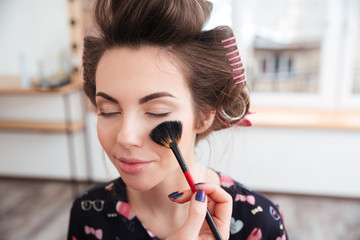 Makeup artist applying brush for face of woman in curlers