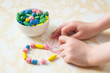 Children's hands collect beads on a string