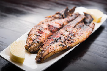 Fish on the grill with lemon on white plate