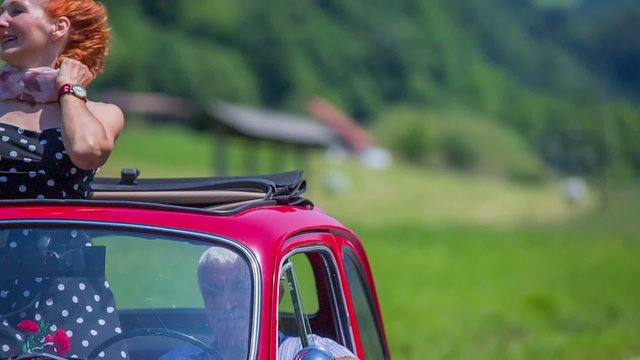 A senior lady standing up straight in a red yugo