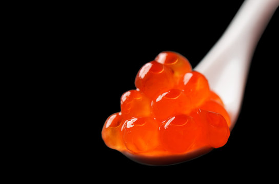 Red caviar in a white ceramic spoon isolated on a black backgrou