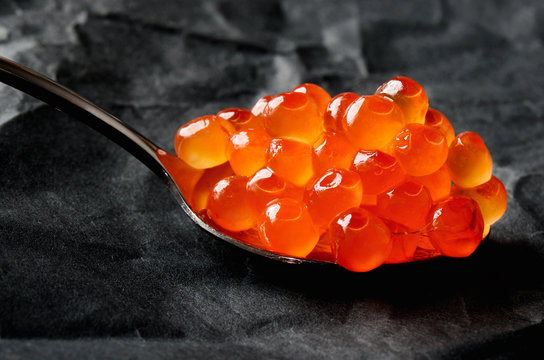 Red caviar in a metal spoon on a black background