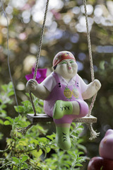Clay doll fat girl sitting on a swing in the garden.