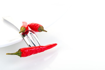 Drei rote Chilischoten mit Gabel auf einem Teller vor weißem Hintergrund