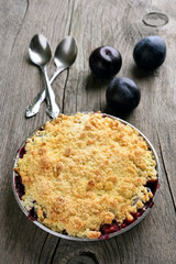 Plum crumb tart in pan on wooden background